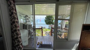 A room with a sliding glass door leading to a deck with outdoor furniture and a view of a lake. - Vacation Stay at Hubbard Lake Air-Conditioned Lakefront Mobile Home (Hubbard Lake)