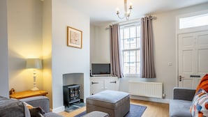 Ein modernes Wohnzimmer mit grauen Sofas, einem Kamin, einem Fernseher und einem Fenster mit Vorhängen.