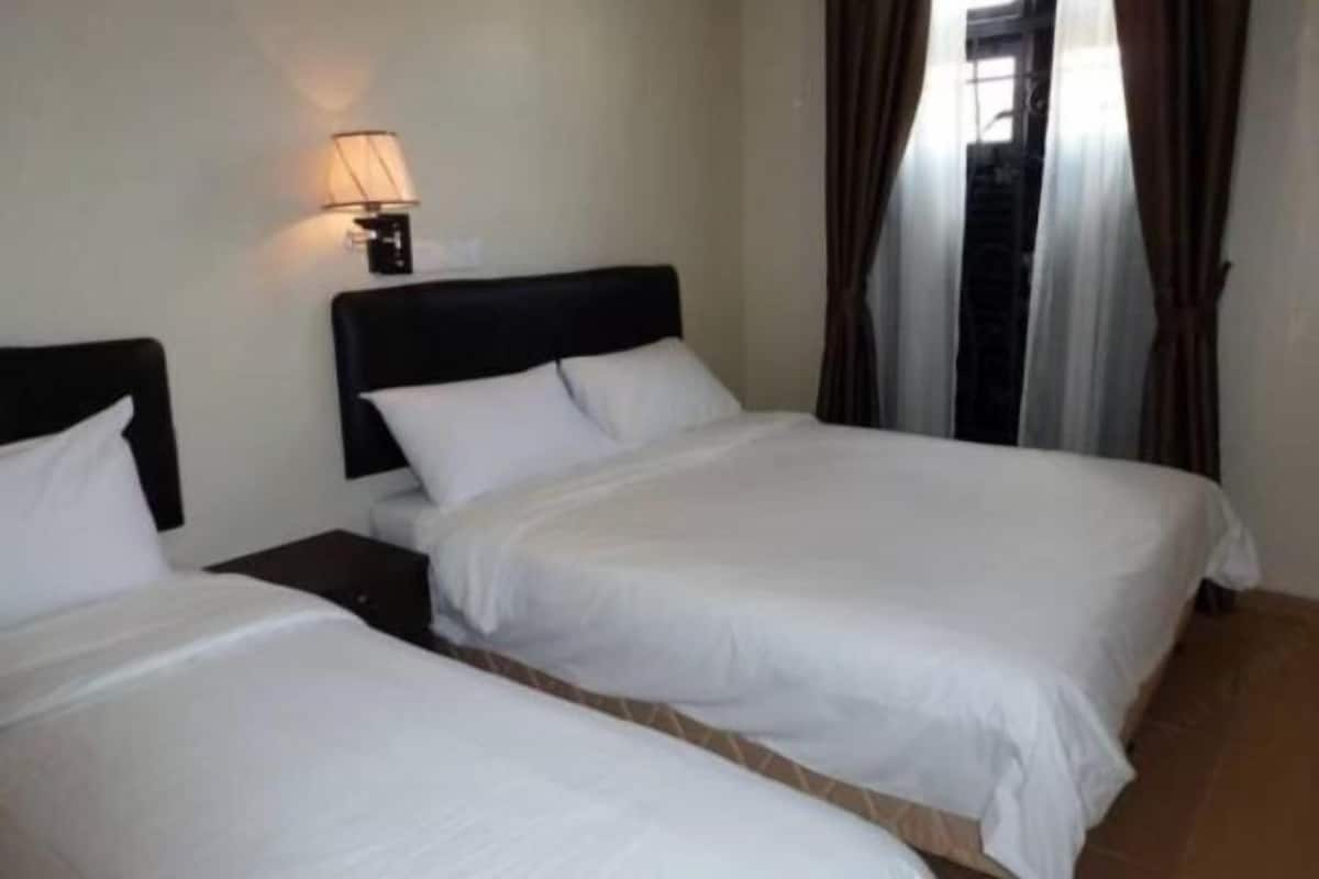 A hotel room with two beds, a nightstand, a lamp, and a view of a building outside.