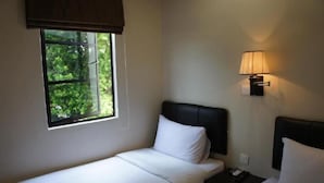 Ein Einzelbett mit weißer Bettwäsche, ein Nachttisch mit einer Lampe und ein Fenster mit Blick ins Grüne.