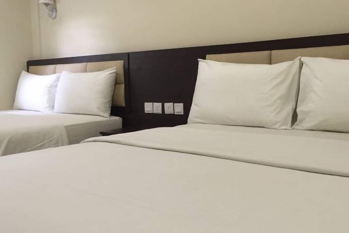 A hotel room with two beds, a dark headboard, and a wall-mounted light fixture.