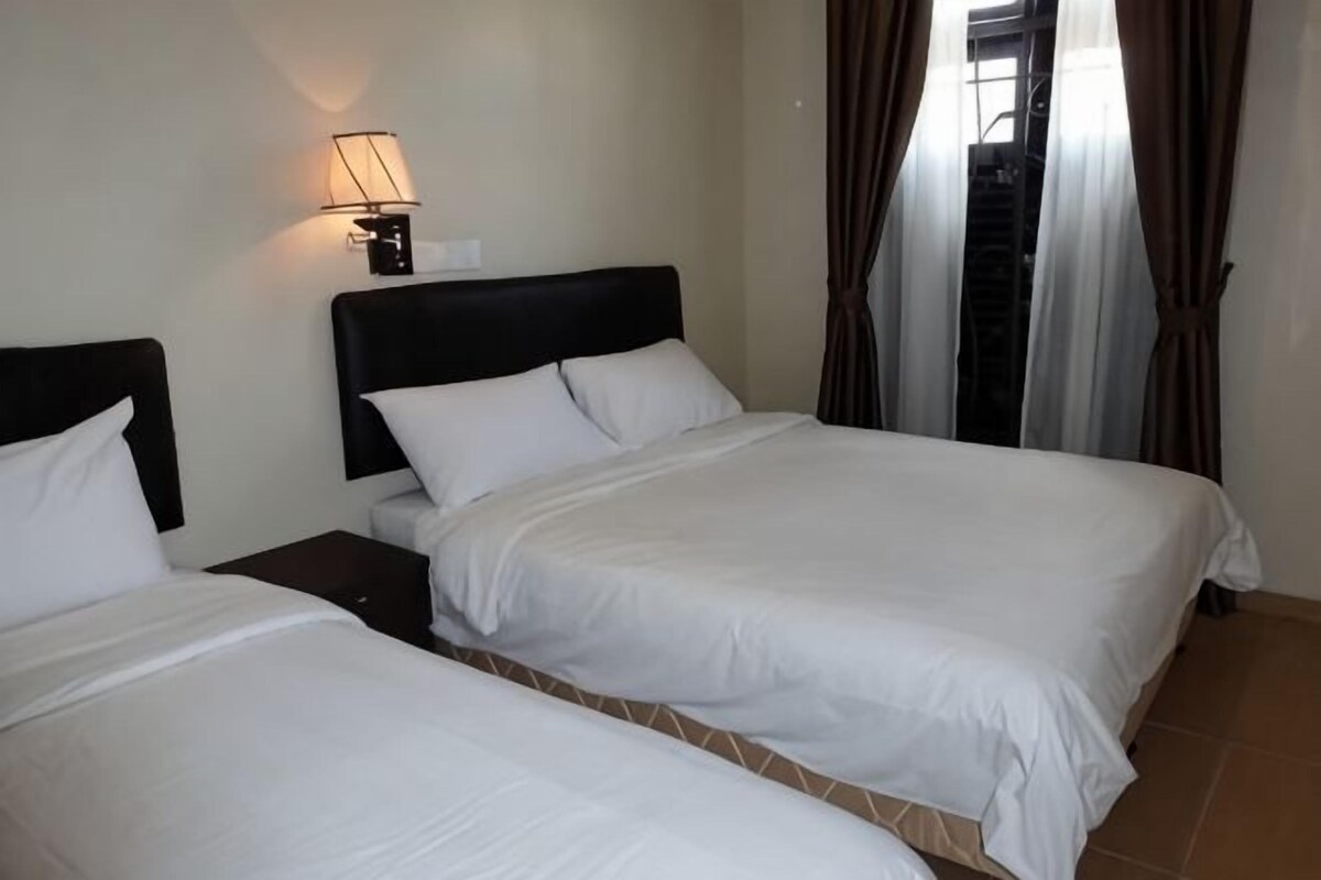 A hotel room with two beds, a nightstand, a lamp, and a window with curtains.