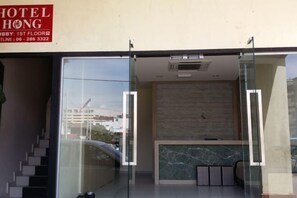 Welcome to Hotel Hong, where guests can check in at the reception desk through a glass partition and access upper floors via the staircase.