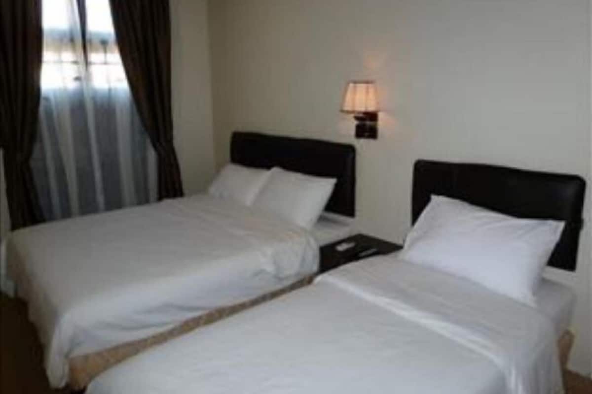 A hotel room with two beds, a nightstand, a lamp, and a window with curtains.