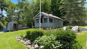 A small, single-story house with a porch, surrounded by a well-maintained garden with rocks and various plants.