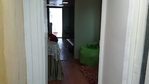 Ein Flur mit einer Zimmerpflanze, einer Bank und einer Tür zu einem Raum mit einem Bett und einem Sessel.