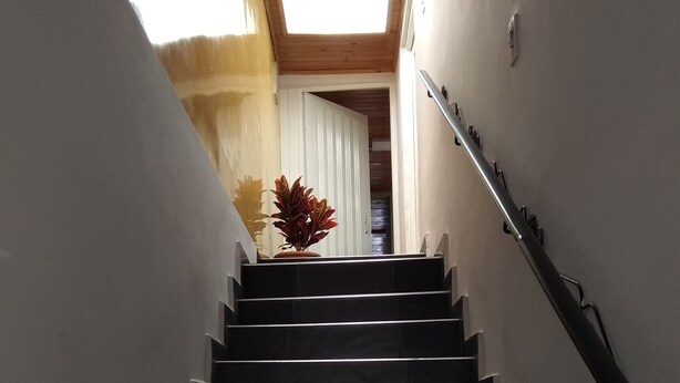 Eine Treppe mit schwarzen Stufen und einem Geländer, die zu einem Raum mit Holzboden und einem Oberlicht führt.
