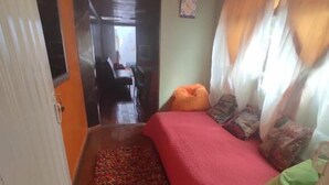 Ein schmales Zimmer mit einem Bett, einem kleinen Teppich und einer Tür zu einem weiteren Raum.