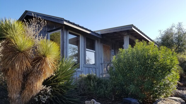 Una casa de madera con porche, rodeada de plantas y rocas propias del desierto.