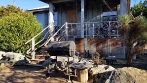 Una cabaña rústica con porche, una parrilla y una rueda de madera.