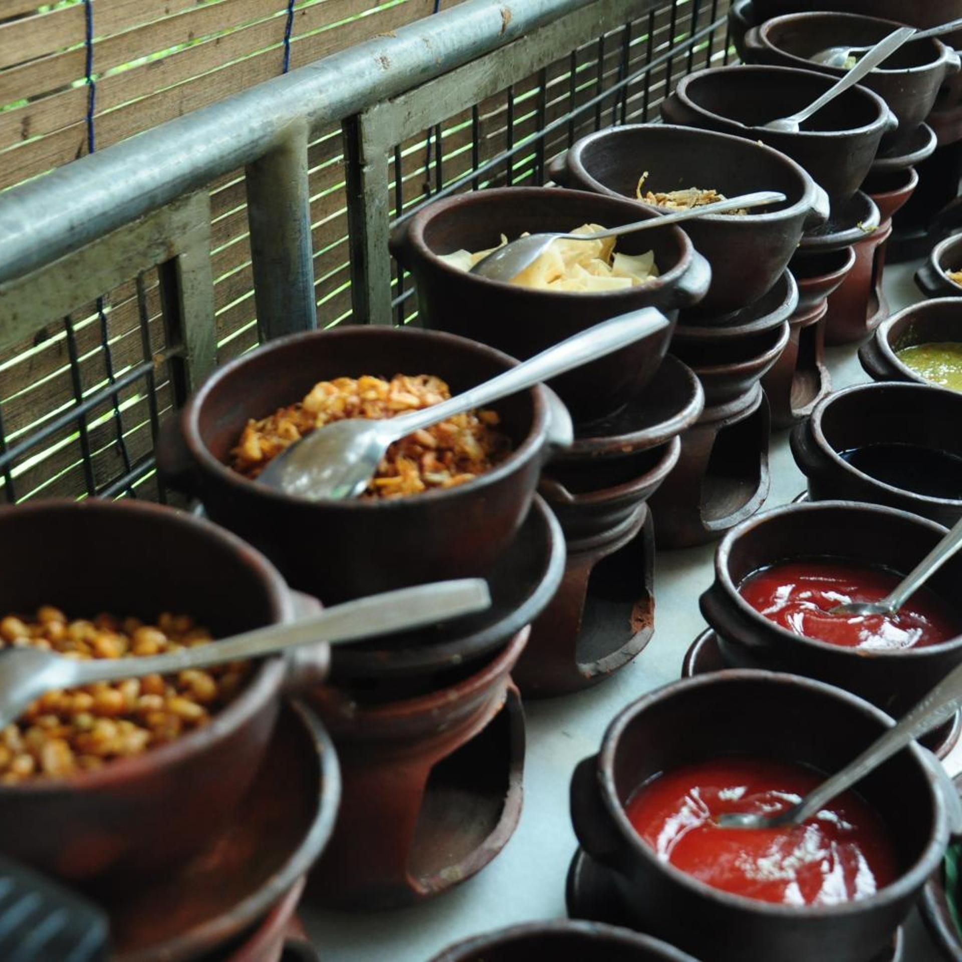 A variety of food items in small ceramic bowls, some with spoons, arranged on a table.