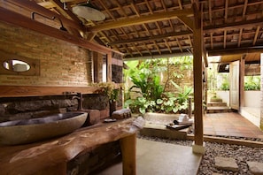 A rustic bathroom with a large stone sink, wooden beams, and a brick wall. - Desa Alamanis Resort Vila (Beber)