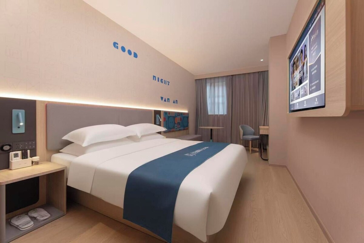 Una habitación de hotel moderna con una cama grande, mesitas de noche, un escritorio y un televisor montado en la pared.