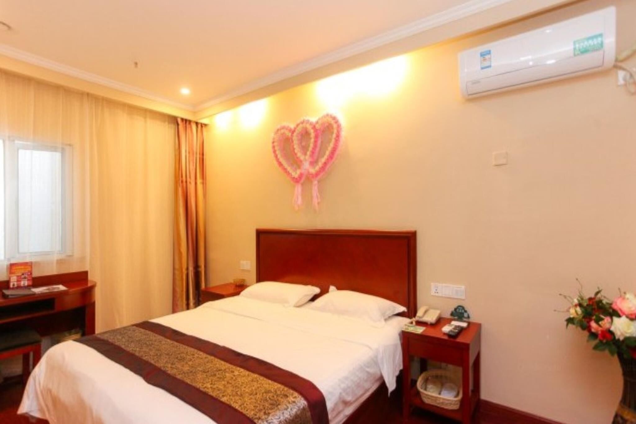 A hotel room with a bed, bedside tables, a desk, an air conditioner, and a wall decoration.