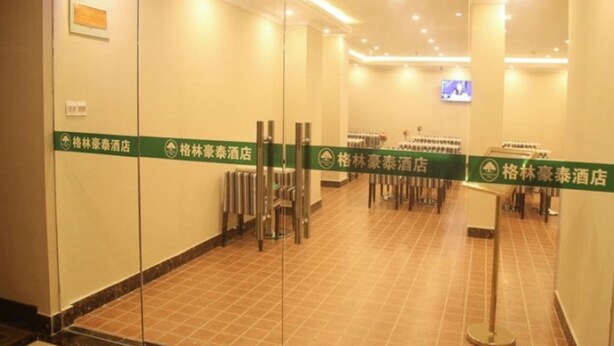 Un vestíbulo de hotel con piso de baldosas, puertas de vidrio y un letrero verde que muestra el nombre del hotel.