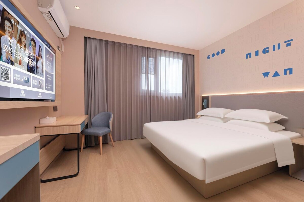 Una habitación de hotel con cama, escritorio, silla y televisor instalado en la pared.