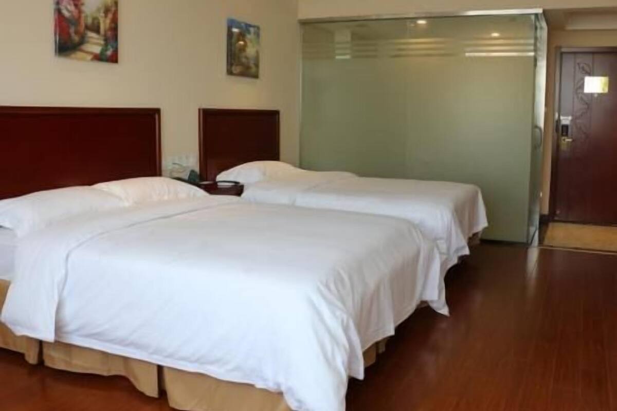 A hotel room with two beds, a wooden headboard, a door, and a wall with two paintings.