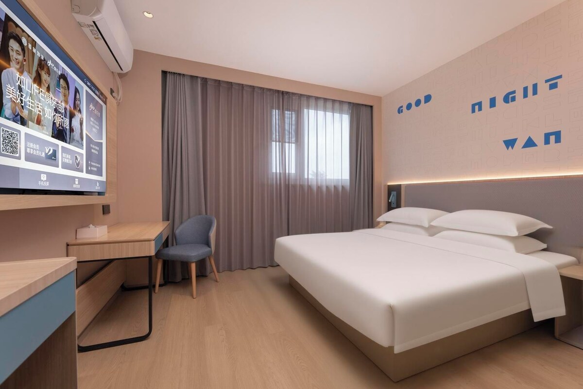 Una habitación de hotel moderna con cama, escritorio, silla y televisor montado en la pared.