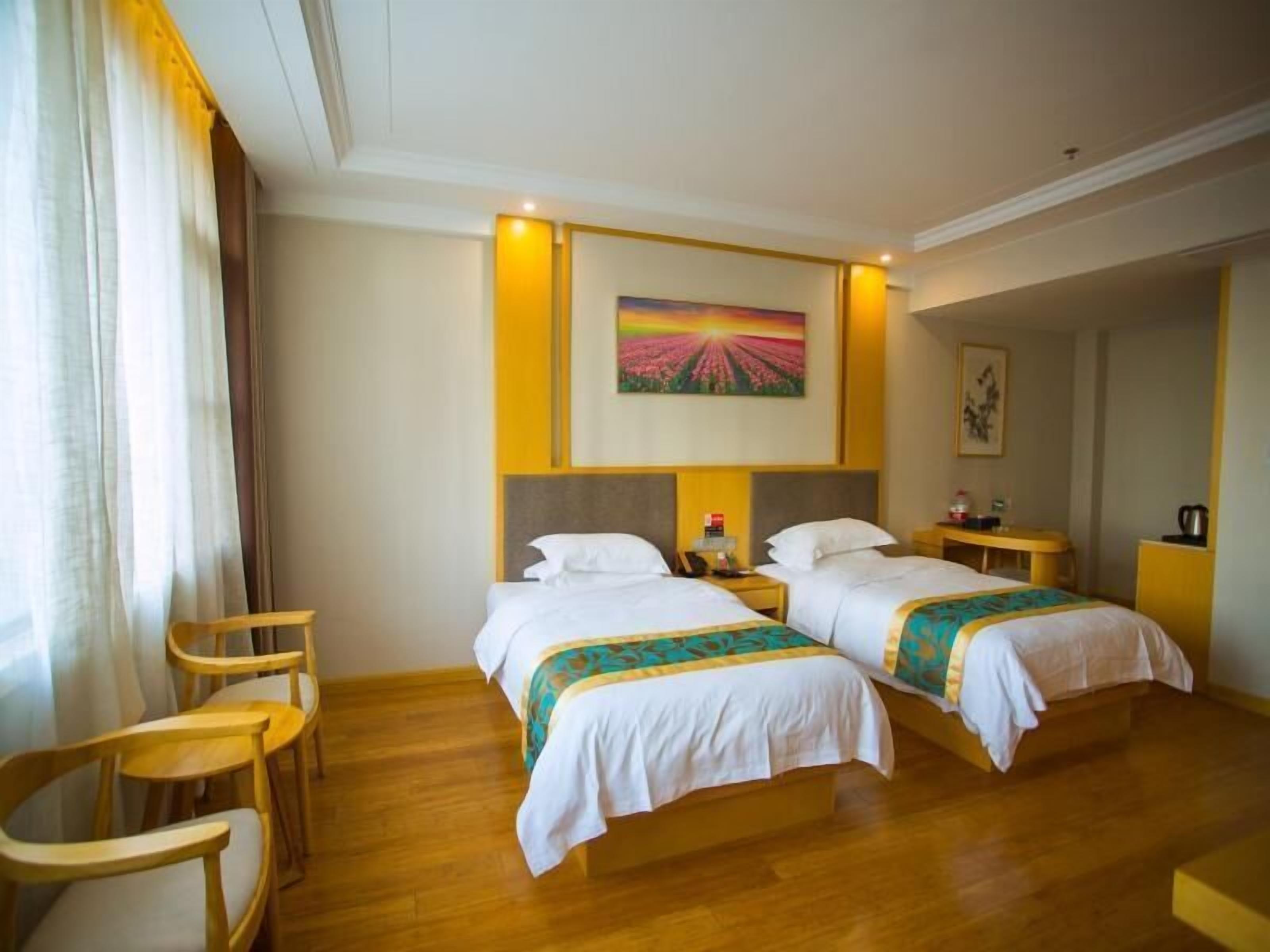 A hotel room with two beds, wooden chairs, a small table, and a painting on the wall.