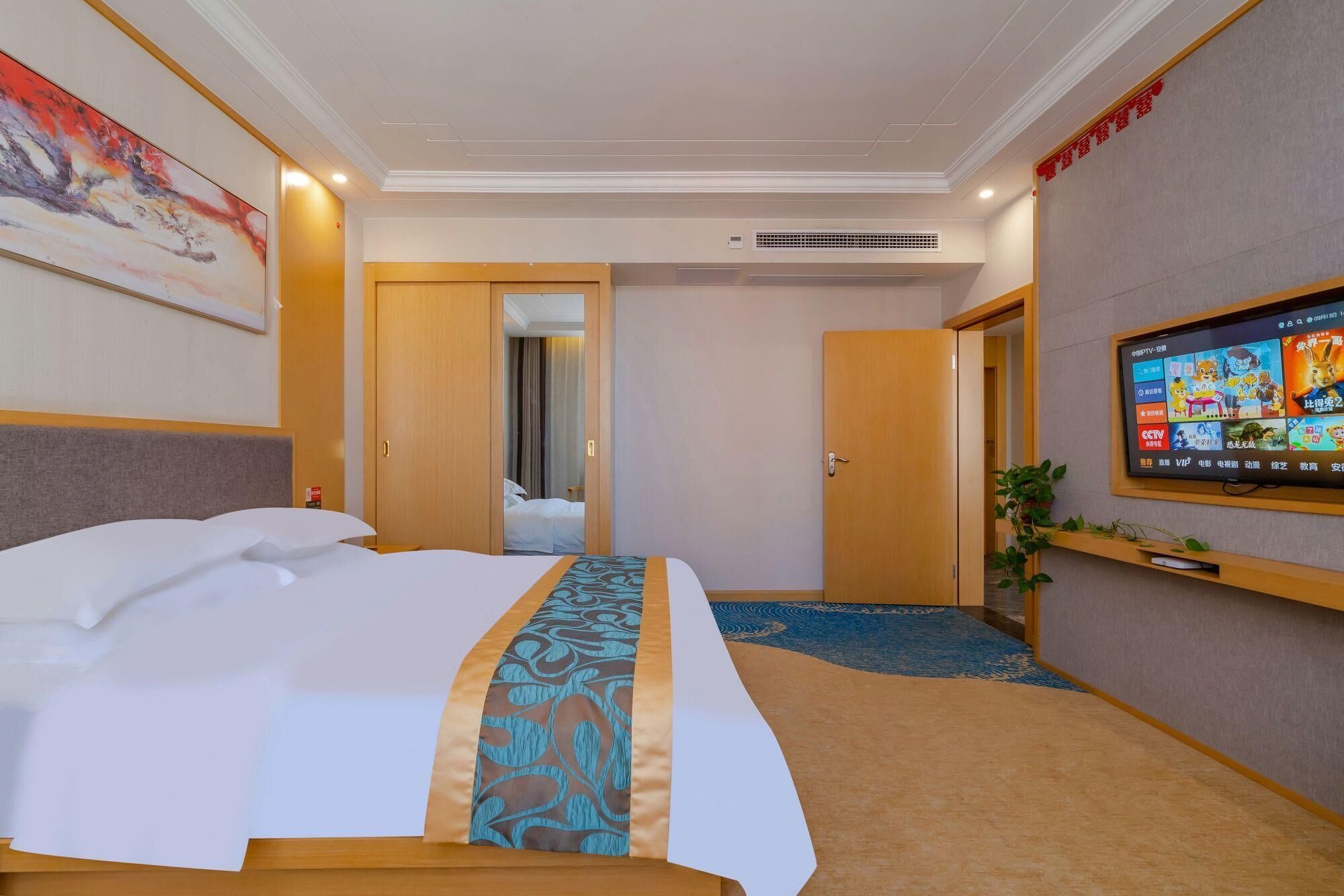 Una habitación de hotel con una cama, un televisor montado en la pared y una puerta que da a otra estancia.