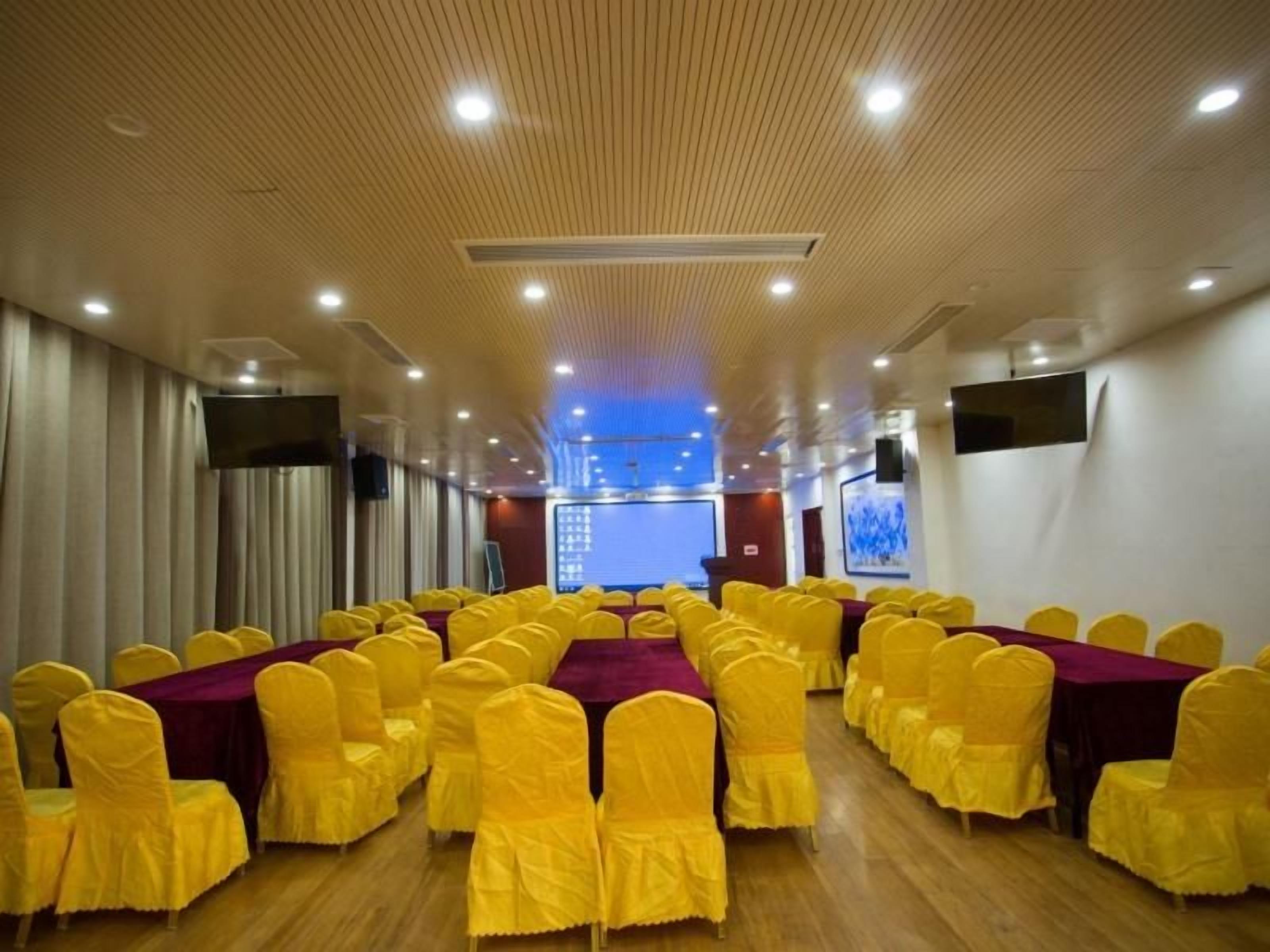 A conference room with rows of yellow chairs, a large screen at the front, and a wooden ceiling.