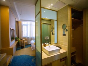 A hotel room with a large window, a bed, a desk with a chair, a bathroom with a sink and mirror, and a blue carpet. - Greentree Eastern Fuyang Yingdong District South (Fuyang)