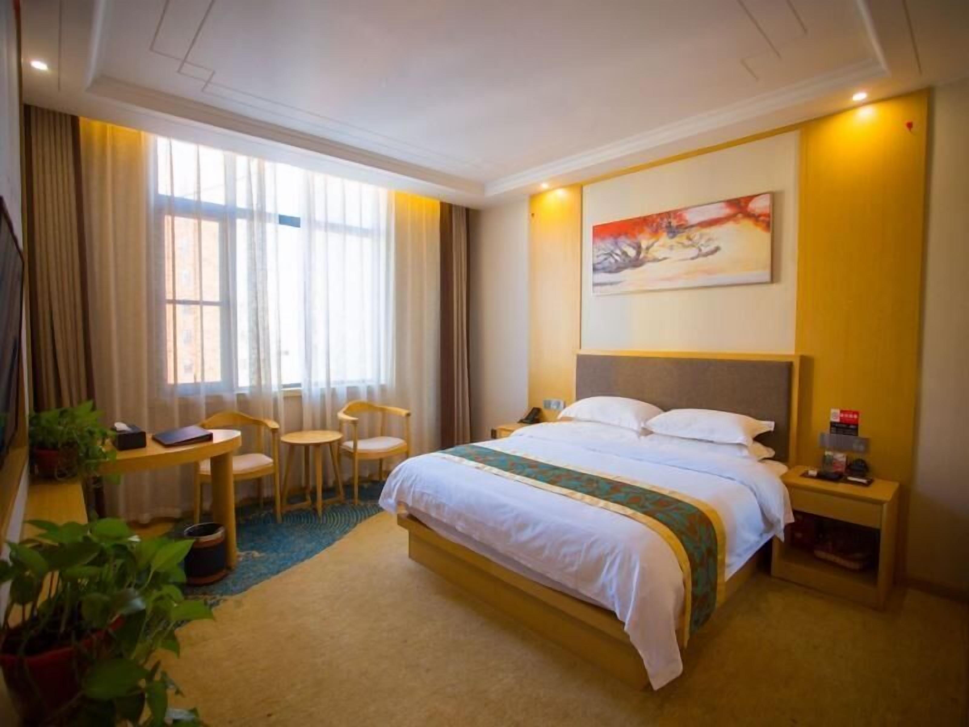 A hotel room with a large bed, a desk with chairs, a small table, and a painting on the wall.