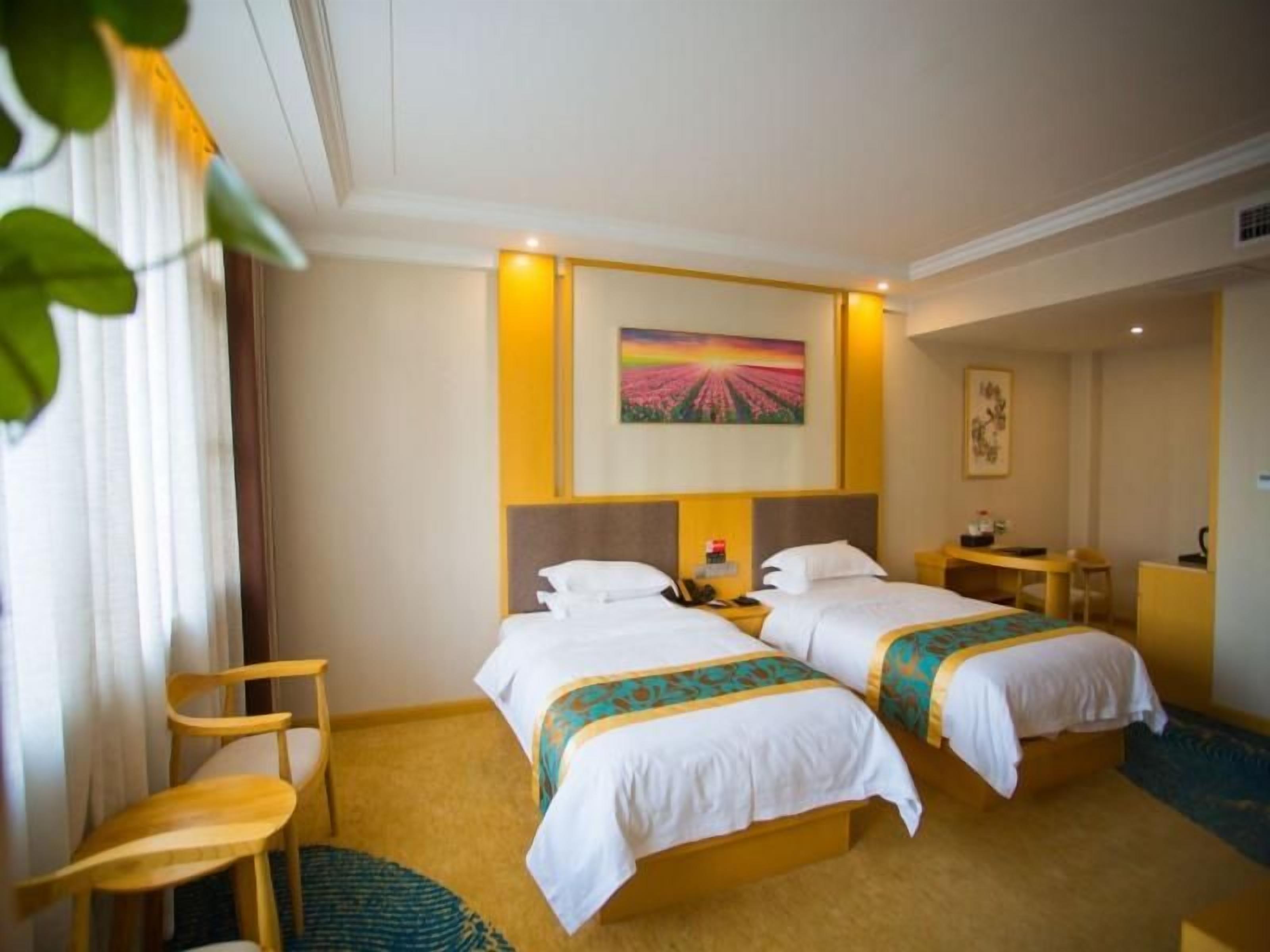A hotel room with two beds, a desk, a chair, and a painting on the wall.