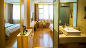 Habitación de hotel con cama, escritorio, silla, mesita, espejo y baño con lavamanos y espejo.