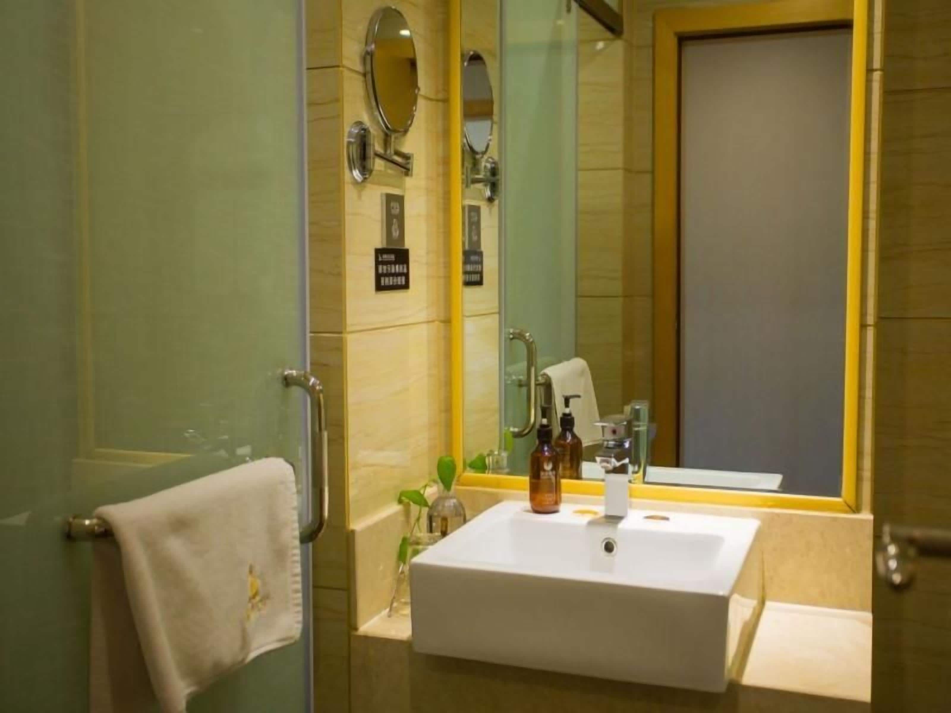 A bathroom with a glass shower door, a white sink with a mirror above it, and toiletries on the sink.