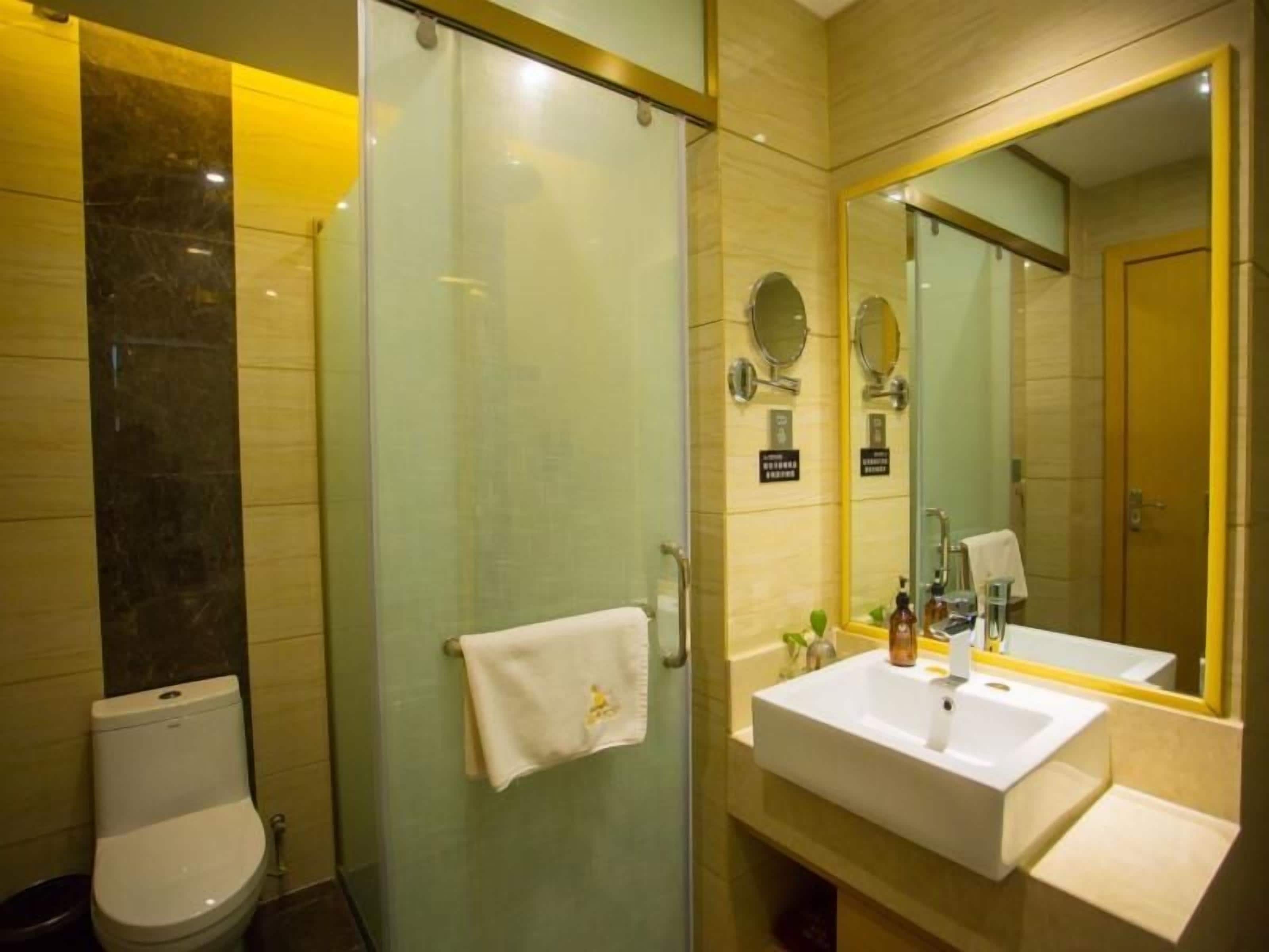 Un baño con cabina de ducha de vidrio, inodoro, lavamanos con espejo y una toalla colgada en la pared.