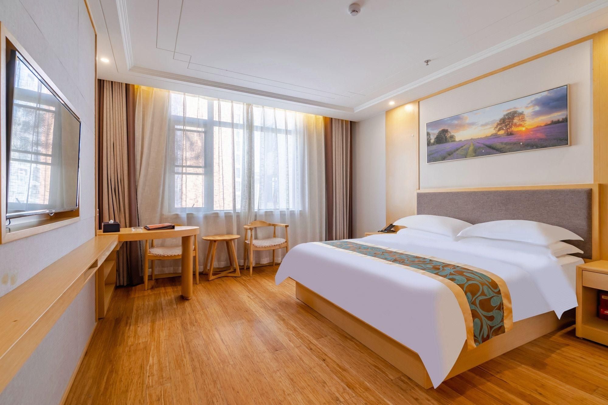 Una habitación de hotel con una cama grande, un escritorio con sillas, un televisor y un cuadro en la pared.
