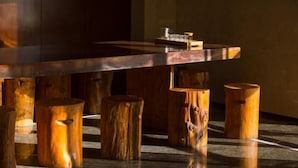 Una mesa de comedor de madera con superficie reflectante, sostenida por patas cilíndricas de madera.