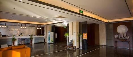 A modern hotel lobby with a reception desk, seating area, and a decorative wall sculpture.