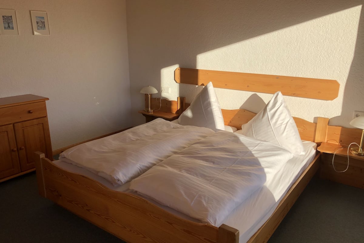 A wooden bed with white linens, two bedside tables with lamps, and a wooden nightstand.