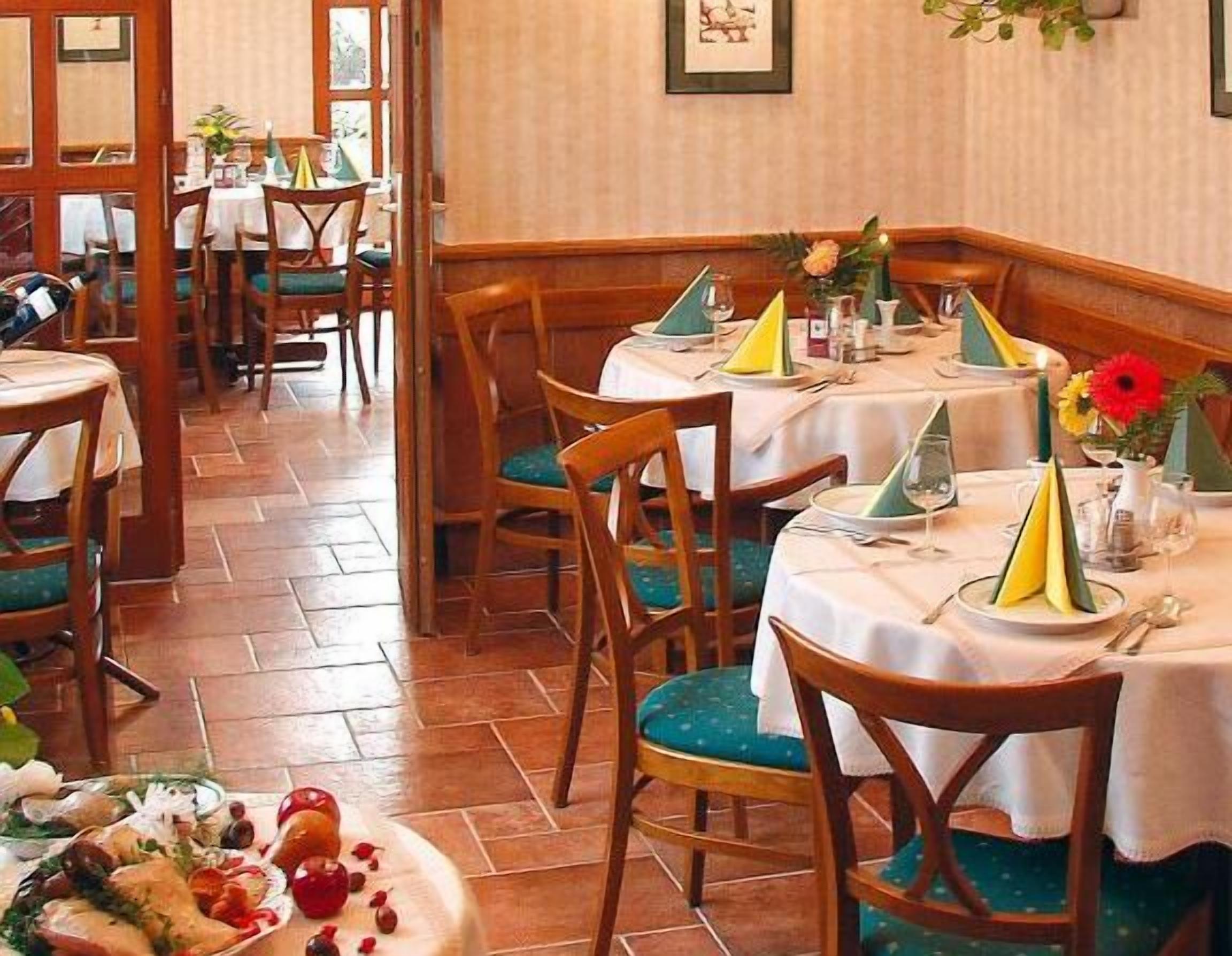 Interior de restaurante con sillas y mesas de madera, algunas con servilletas y cubiertos.
