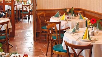 Interior de restaurante con sillas y mesas de madera, algunas con servilletas y cubiertos.