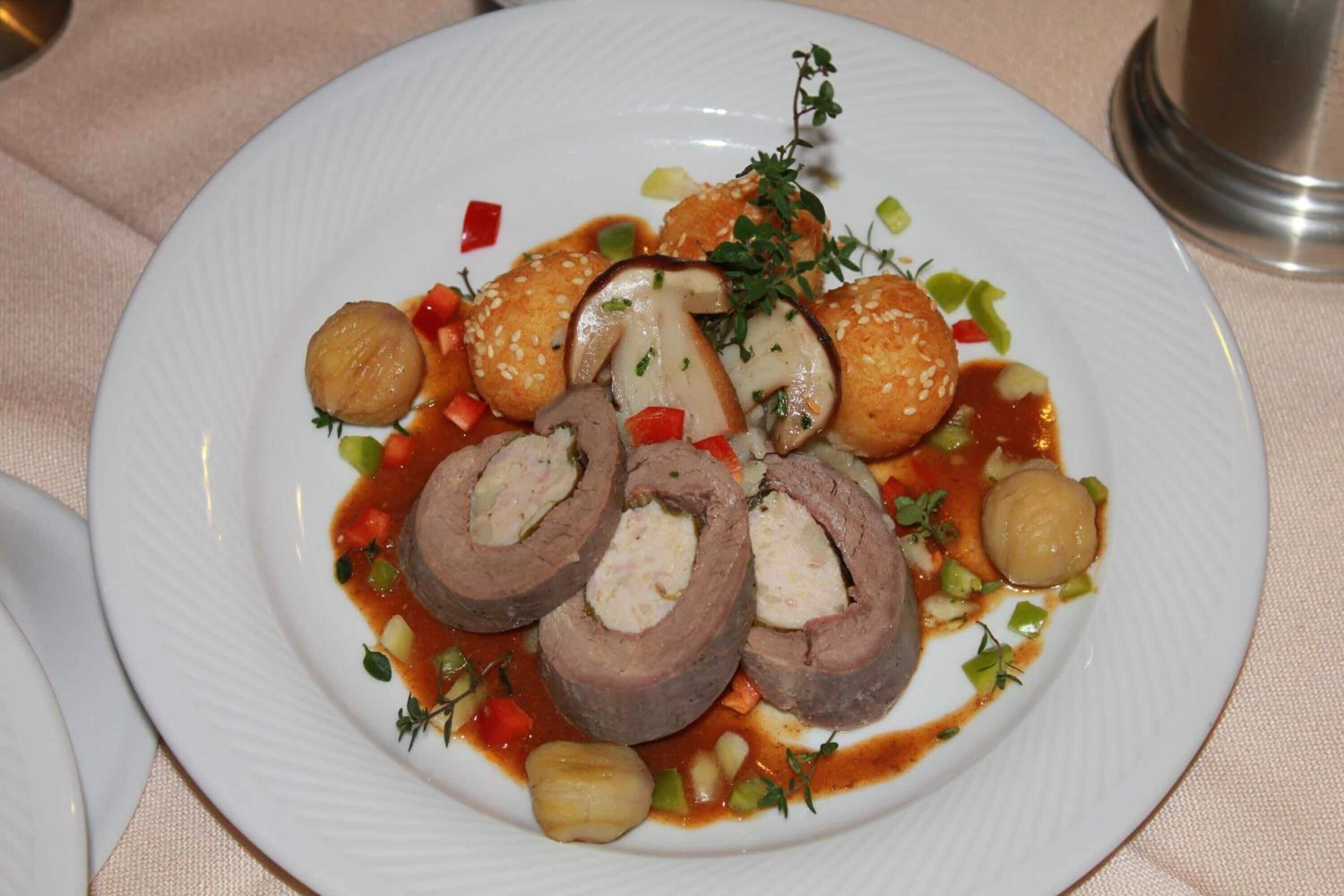 Um prato de comida com carne enrolada, bolinhos e legumes.