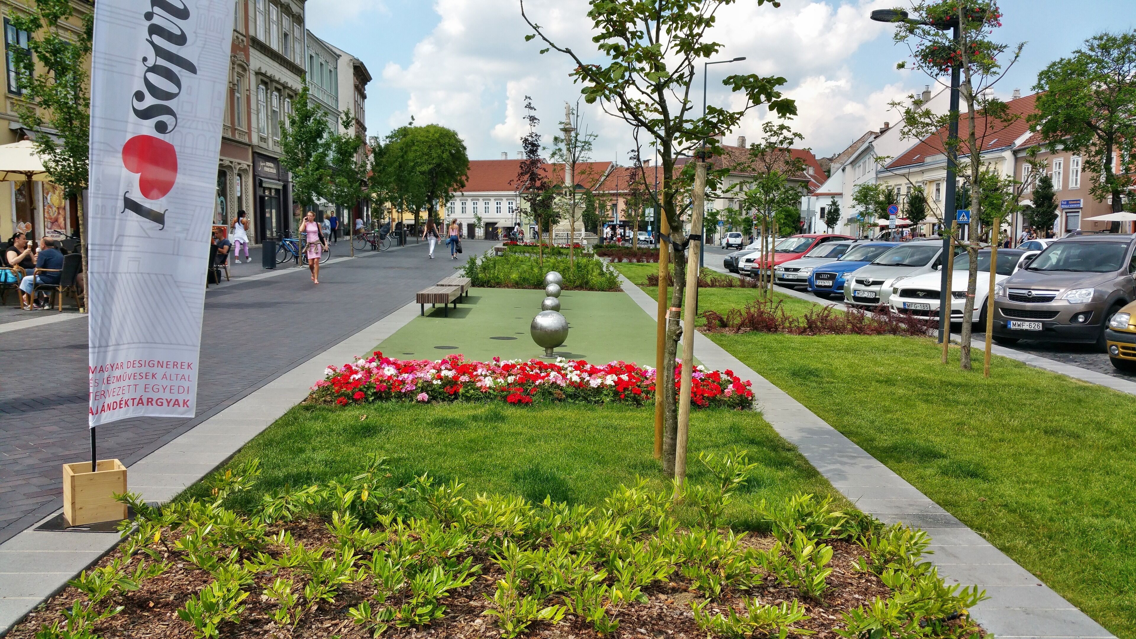 A public square with a flower bed, benches, and a banner.