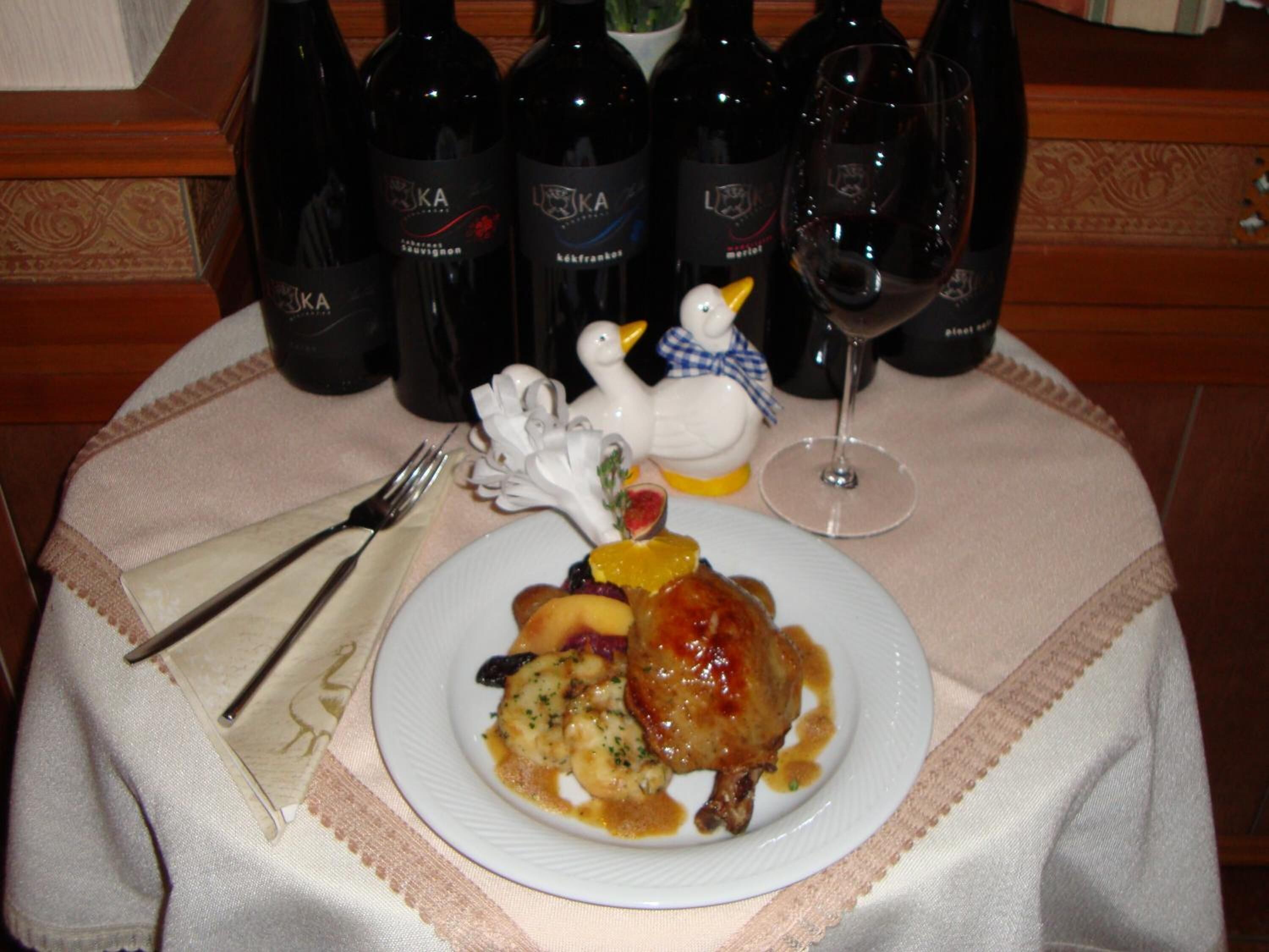 Une table avec une assiette de nourriture, des bouteilles de vin, un verre de vin et une figurine de canard décorative.