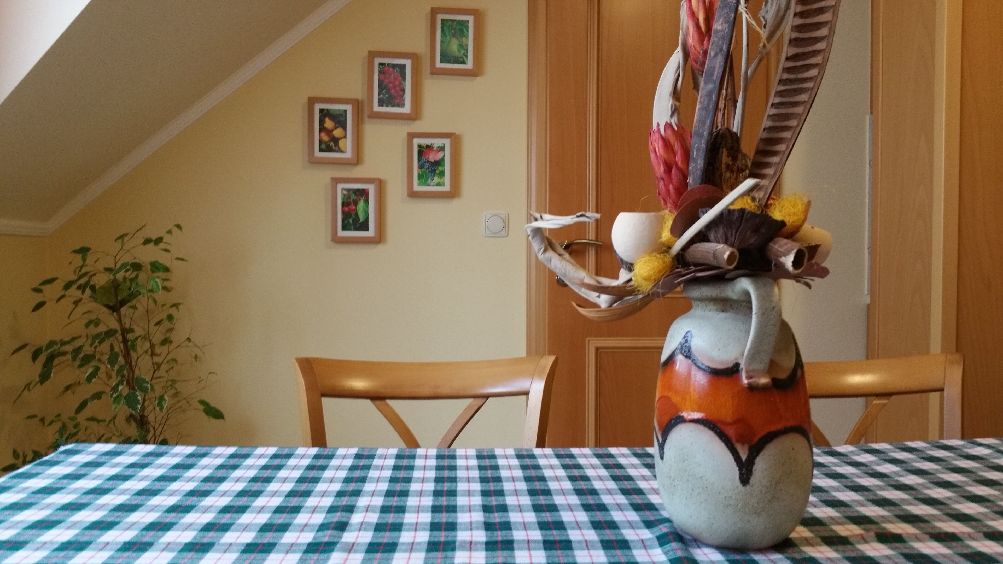 Une table à manger recouverte d’une nappe à carreaux, un vase agrémenté d’une composition florale et une chaise en bois.