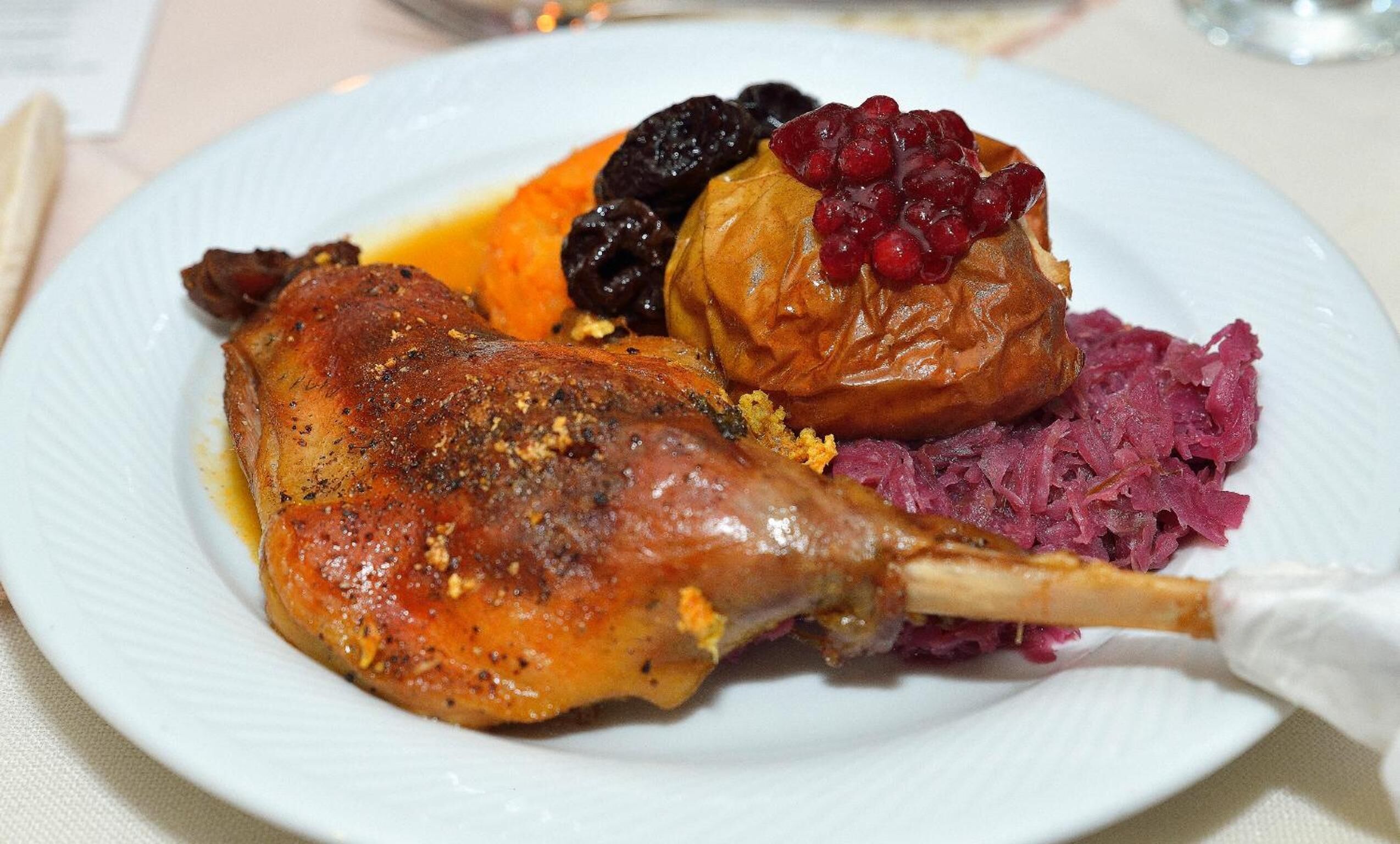A plate with a roasted leg of lamb, a baked fruit, and a side of red cabbage.