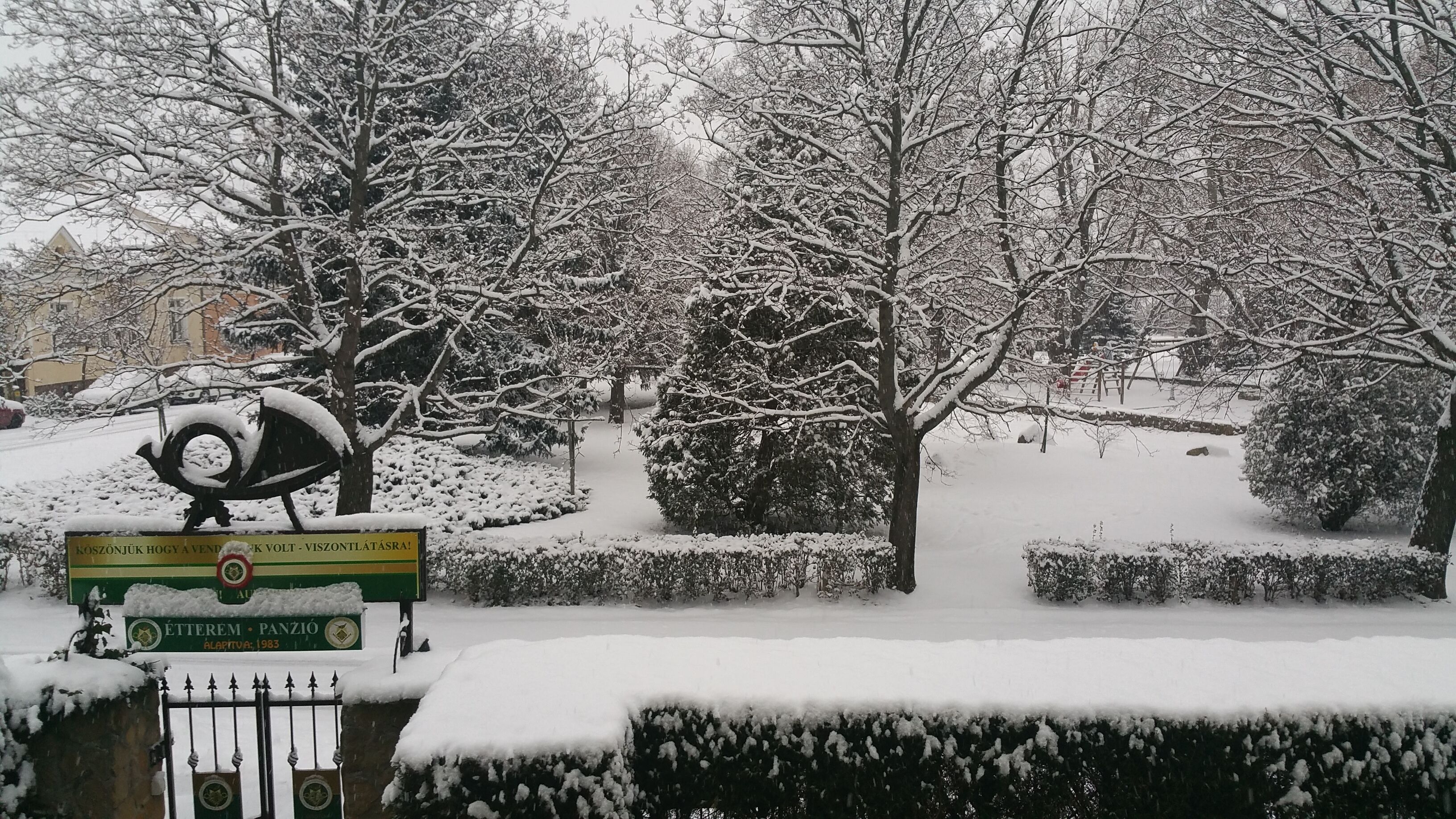 A snow-covered park with a statue, a sign, and a building in the background.