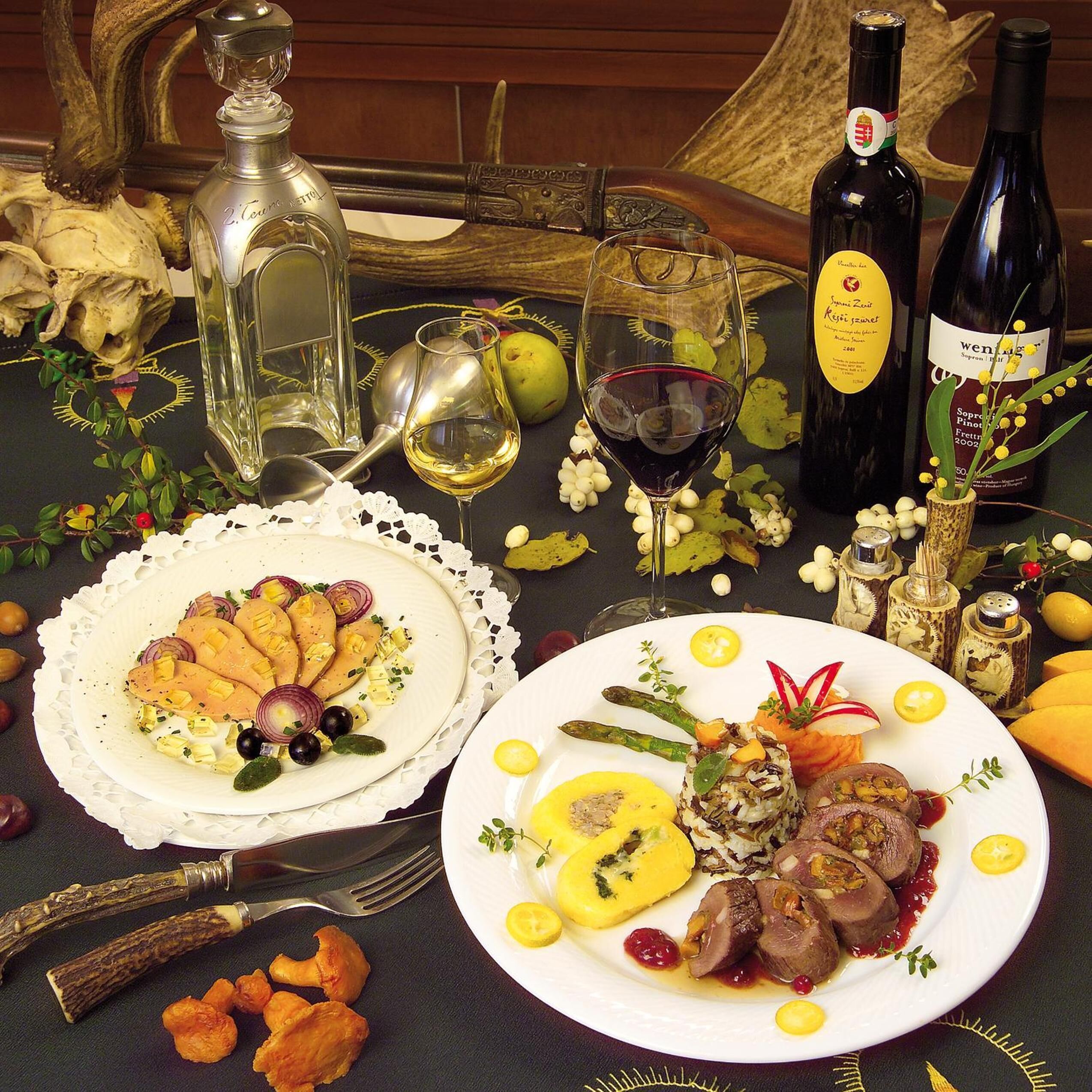 A dining table with two plates of food, wine bottles, and a decorative centerpiece.
