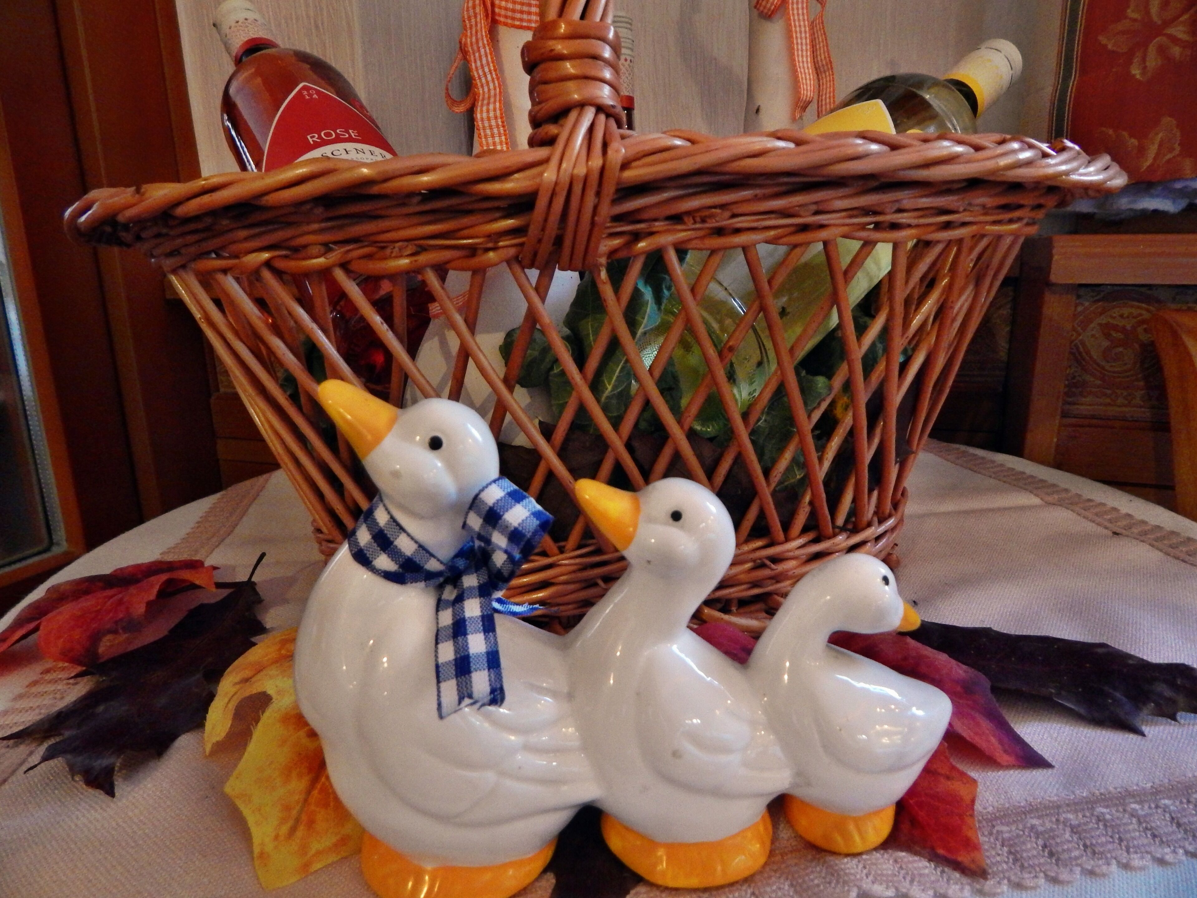 Een decoratieve rieten mand met twee witte keramieken eendjes, waarvan één een blauw geruit boogband heeft.