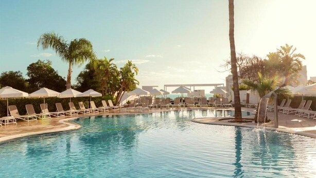 A pool area with lounge chairs and umbrellas, surrounded by palm trees. - Lantiana Gardens (Paralimni)