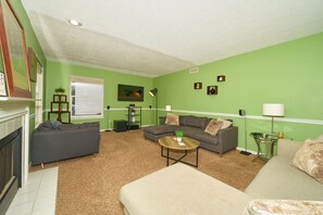 A living room with green walls, a fireplace, a grey sofa, a beige sofa, and a coffee table. - Beautiful modern home just 20 mins from downtown Indy & 25 mins from Grant Park (Indianapolis)