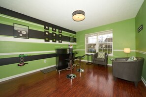 A room with green walls, a black and white striped accent wall, a bar area with stools, a grey sofa, and a window with a view of the outside. - Beautiful modern home just 20 mins from downtown Indy & 25 mins from Grant Park (Indianapolis)