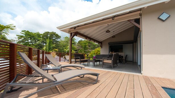 Une terrasse en bois avec des chaises longues et une table, un patio couvert et une piscine.