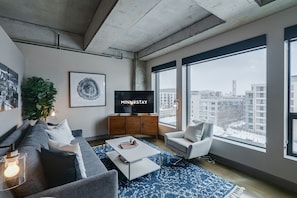 Un salon moderne avec une grande fenêtre, un canapé, une table basse, un téléviseur et une plante.